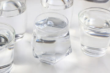 Clear drinking water in various glass cups arranged on a white surface.