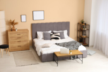 Interior of stylish room with comfortable bed, bench with laptop, chest of drawers and shelving unit