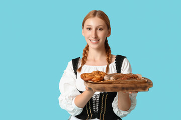 Beautiful happy Octoberfest waitress with board of traditional food on blue background