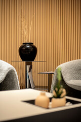 Elegant lounge area detail with a black vase on a modern side table against a fluted wood wall, embodying sophisticated, minimalist interior design. © Okta