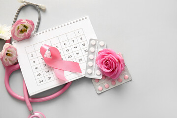 Composition with pink ribbon, calendar, pills and flowers on grey background. Breast cancer...
