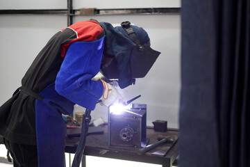 Welder performing Tungsten Inert Gas welding process (TIG) on stainless steel. TIG welding uses the heat generated by an electric arc struck between a non-consumable tungsten electrode and the work