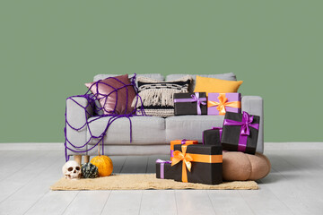 Cozy sofa with gift boxes for Halloween, pumpkin and skull near green wall