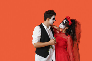 Young couple dressed for Halloween with rose on orange background