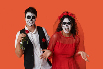 Young couple dressed for Halloween with rose on orange background