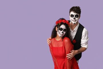 Young couple dressed for Halloween on lilac background