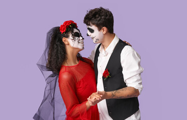 Young couple dressed for Halloween dancing on lilac background