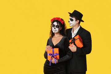 Young couple dressed for Halloween with gift boxes on yellow background