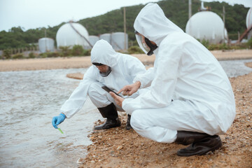Scientists collect water samples in protective gear near industrial storage tanks during a research...