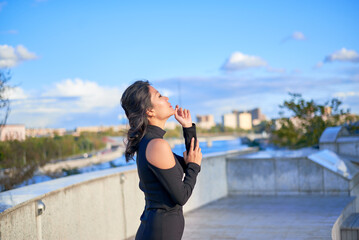 A woman is standing on a balcony and pointing to the sky. She is wearing a black dress