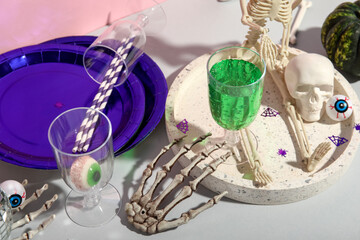 Glass of tasty cocktail, tableware and decorations for Halloween on grey background
