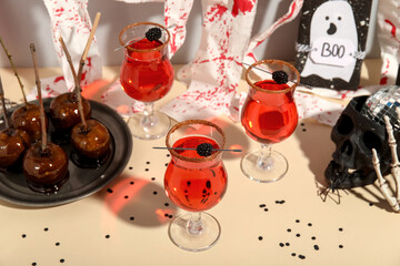 Glasses of cocktails, tasty caramel apples and decorations for Halloween on color table