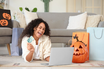 Young African-American woman with credit card and laptop shopping online for Halloween at home