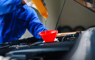 Mechanic pouring engine oil into car engine. Oil change service, car repair, engine inspection and maintenance.