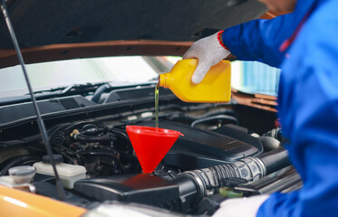 Mechanic pouring engine oil into car engine. Oil change service, car repair, engine inspection and maintenance.