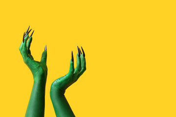 Green hands of witch on yellow background. Halloween celebration