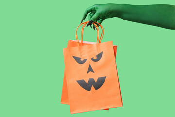 Green hand of witch with shopping bags on color background. Halloween celebration
