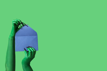 Green hands of witch with envelope on color background. Halloween celebration