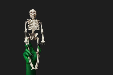 Green hand of witch with skeleton on black background. Halloween celebration