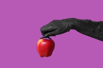Black hand of witch with fresh apple on purple background. Halloween celebration