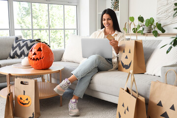Young woman with credit card and laptop shopping online for Halloween at home