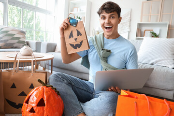 Happy young man with bag and credit card shopping online for Halloween at home