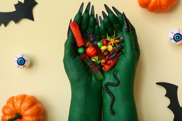 Witch's hands with different candies and decorations for Halloween on color background, closeup