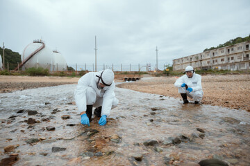 Two men in protective gear collect water samples from forest stream. Environmental scientists...