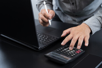 Businessman calculating financial data using calculator and laptop with digital pen for online accounting task