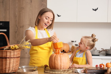 Cute little girl with her mother carving Halloween pumpkin in kitchen