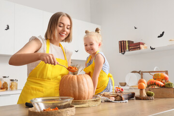 Cute little girl with her mother carving Halloween pumpkin in kitchen