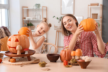 Cute little girl with her mother carving Halloween pumpkins at home