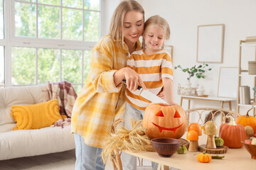 Happy mother with her little daughter carving Halloween pumpkin at home