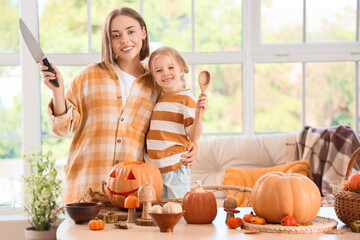 Happy mother with her little daughter carving Halloween pumpkin at home