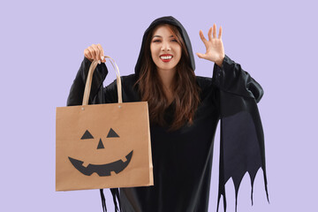 Young Asian woman dressed for Halloween with shopping bag on lilac background