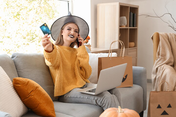 Young woman in witch hat with credit card shopping online for Halloween at home