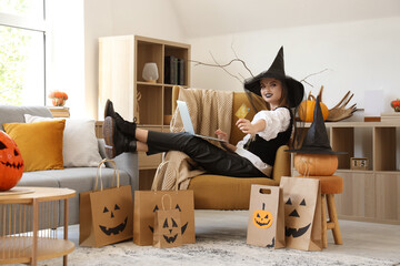Young woman dressed for Halloween as witch with credit card and laptop shopping online at home