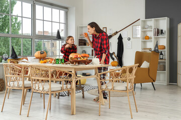 Cute little girl with her mother carving Halloween pumpkin on table at home