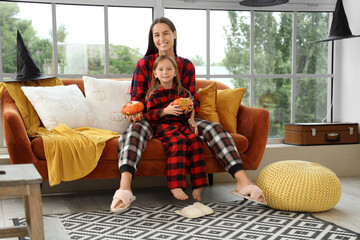 Cute little girl and her mother with Halloween pumpkins sitting on sofa at home