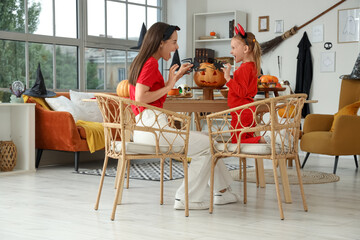 Scary little girl with her mother carving Halloween pumpkin at home