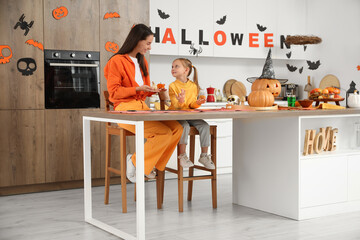 Little girl and her mother with Halloween pumpkins at table in kitchen