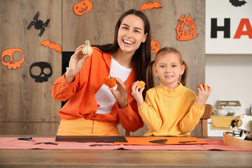 Little girl and her mother with Halloween pumpkins at table in kitchen