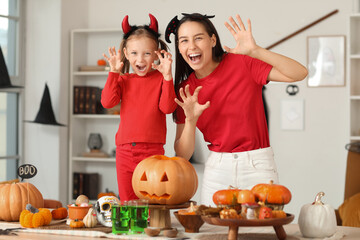 Happy mother and her little daughter with Halloween pumpkins on table at home