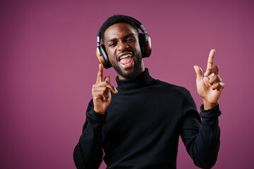 Smiling young Black man enjoying music with headphones, expressing happiness and joy against a...