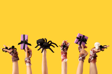 Female bandaged hands with Halloween gifts, skull and spiders on yellow background