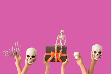 Female hands with Halloween gift, skeleton, hand and skulls on purple background