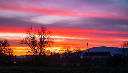 Fototapeta premium Dramatic fiery sunset over a rural landscape with tree silhouettes