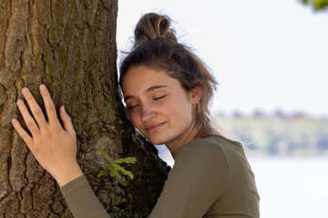 In a peaceful and serene moment, a young woman is embracing a large tree, showcasing her deep...