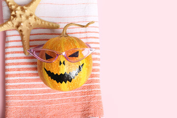 Halloween pumpkin, starfish, towel and sunglasses on pink background