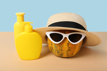 Halloween pumpkin in hat and sunglasses with sunscreen creams on color background